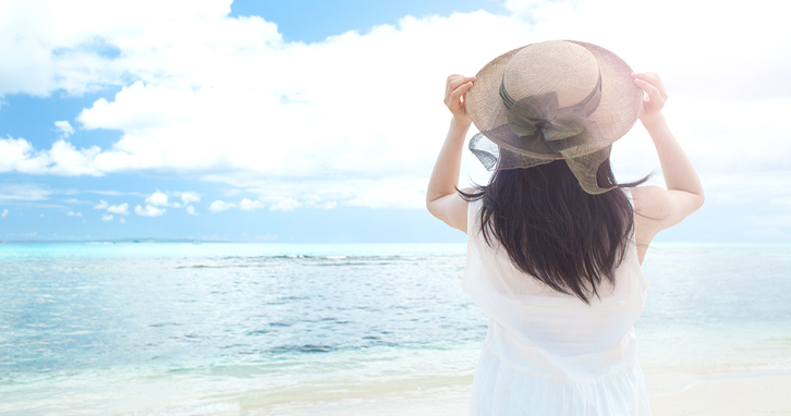 日差しの強い空と、帽子をかぶった後ろ向きの女性のイメージ写真。
